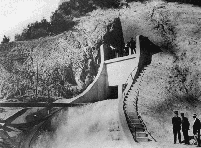 The water gates are now opened to full capacity. The gatemen were rather โhigh-pricedโ help themselves, including Mulhollandโs top assistants: Roderick Mackay, chief construction engineer; H. A. Van Norman, Owens Valley division engineer; D. L. Reaburn, Saugus division engineer; A. C. Hansen, Jawbone Division engineer. The fifth man was Adna R. Chaffee, Jr.,
U. S. Army.*