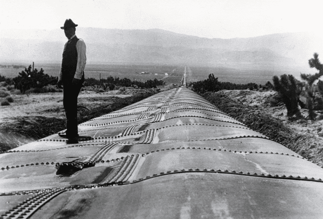 (1914)*^ โ View showing William Mulholland standing on a section of the Antelope Siphon damaged by a major flood. Note: Water pressure alone would restore the pipe to its original circular form.